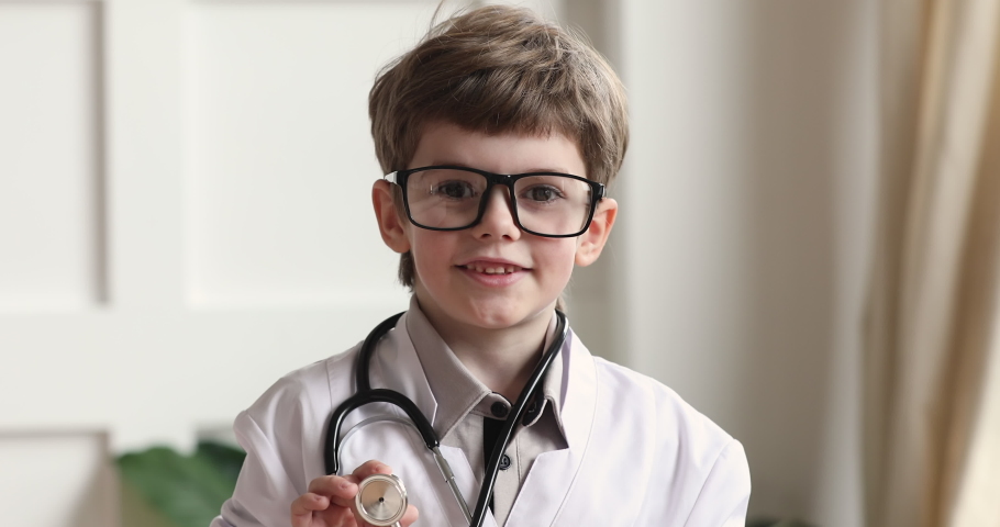 Happy funny adorable cute little preschool child boy wear white medical coat glasses holding stethoscope looking at camera playing doctor alone, children future professions concept, closeup portrait | Shutterstock HD Video #1044921055