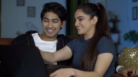 Cute happy couple watching funny videos on a laptop during leisure time in India. Closeup shot of young adorable boyfriend girlfriend happily sitting together on a couch and using the laptop