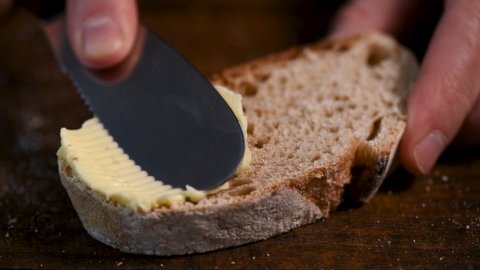 Bread with butter. Knife smearing soft butter on slice of bread, closeup view. Male hands