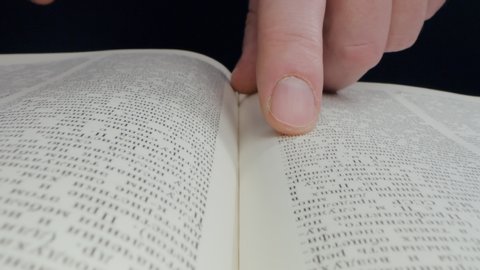 Man is reading a book, close up, isolated. Hand open book for reading. Man is looking for information in book. Close-up macro shot picture of hand and book isolated on black background