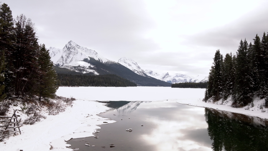 Low aerial shot of frozen Lake with cracks and a high mountain in the distance, Jasper National Park, Alberta Canada