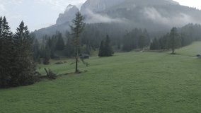 Aerial footage of Dolomites Alps mountains in summer. Rural landscape with farming house, road, pine trees, mountains and low clouds. Geisler or Odle Dolomites Group. Italy