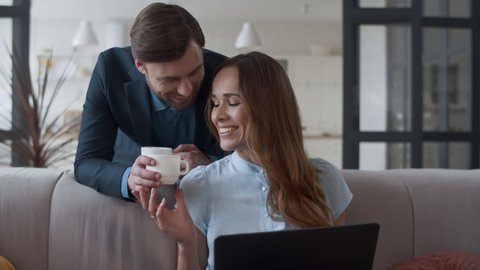 Closeup attractive husband bringing tea cups to wife at home interior. Happy couple making coffee break in livingroom in slow motion. Portrait of smiling woman talking with man at remote workplace.