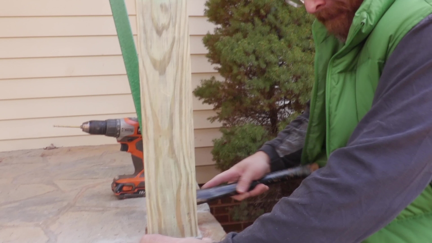 Carpenter lining post up on porch corner.