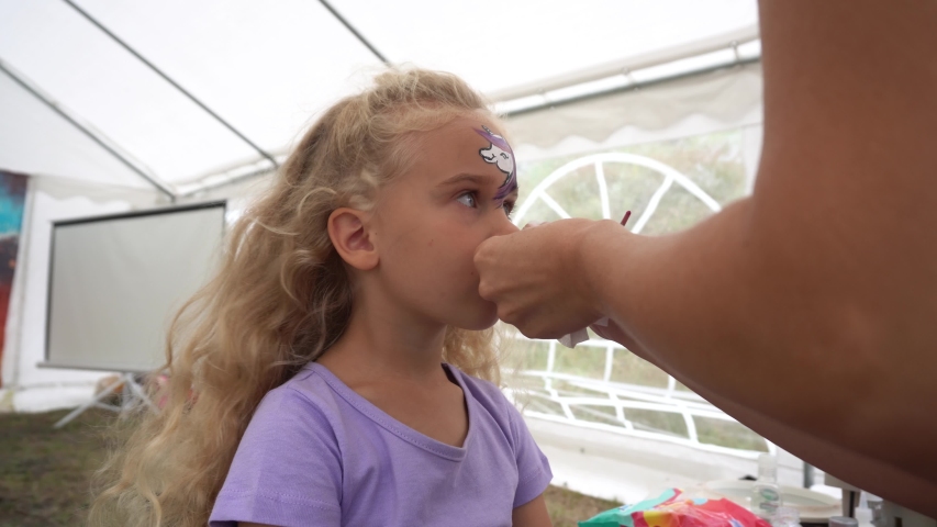 A little girl gets her face painted at a carnival or craft show. Camera motion shot with gimbal.
