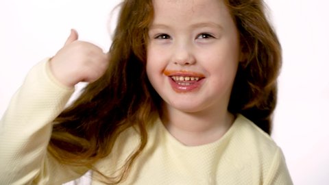 A six-year-old sweet girl just drank tomato juice. The lips of a playful girl are soiled with tomato juice. On the face of the child a happy smile.