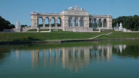 VIENNA AUSTRIA - JULY 11. 2019 wide tripod shot of Schonbrunn / Schonbrunn Palace Gloriette building in soft morning light, foreground green pond with reflections on the water, blue sky, no sound