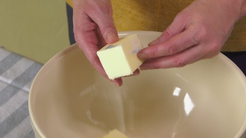Woman baker carefully unwraps half stick of butter over baking mixing bowl and adds butter to ingredients in bowl