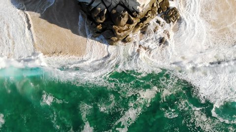 Large waves crash onto rocks and beach in this slow motion drone shot looking down on the breathtaking turquoise water in Baja California Sur