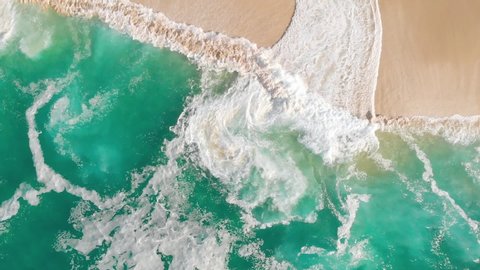 Slow motion drone shot looking straight down at turquoise waves on a beautiful sand beach in Cabo San Lucas, Mexico