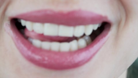 Close view of female mouth: woman is licking lips and showing perfect white teeth