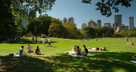 Manhattan, New York - September 21, 2019: People relax on the green lawn of the Sheep Meadow by the apartment and condominium skyscraper residences over the Manhattan skyline in Central Park 
