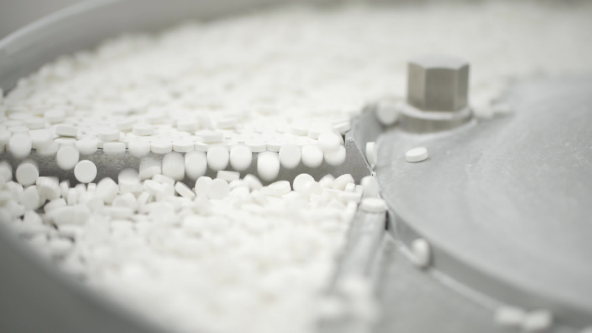 White pills moving on metal automatic line in workshop of pharmaceutical factory. Closeup view of drugs move along conveyor belt during work process in pharma chemical company. Concept: business