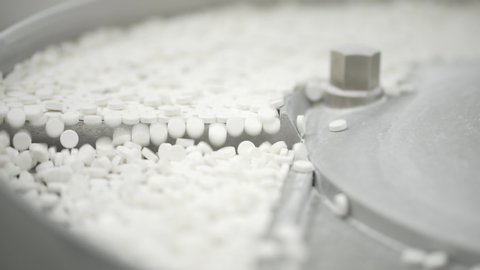 White pills moving on metal automatic line in workshop of pharmaceutical factory. Closeup view of drugs move along conveyor belt during work process in pharma chemical company. Concept: business