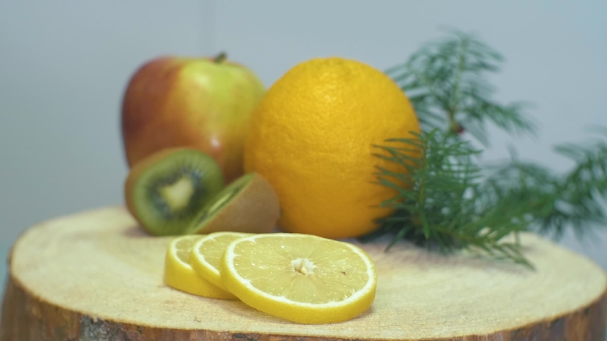 Close up video of camera zooming to the fruits, orange, apple, kiwi and lemon on wooden desk changing focus from lemon to kiwi and apple