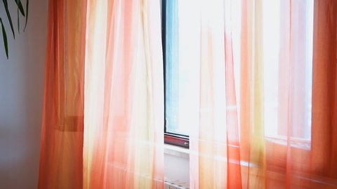 Colorful slow motion of vivid orange open window curtains blinds in room interior indoors apartment flowing in wind in Italy