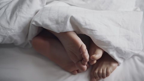 Couple petting in bed. Only feet in the frame. Marriage, family, love, sex concept. Filmed on REd 4k, 10 bit color