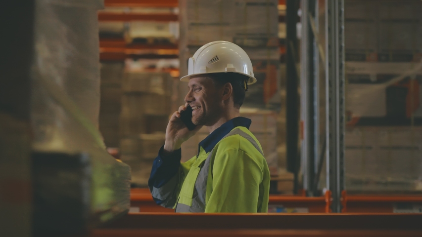 Side view of warehouse manager talking on the phone walking among high shelves with supplies. Storehouse worker having phone call. Merchandiser talking on phone with client walking in warehouse Royalty-Free Stock Footage #1045011478