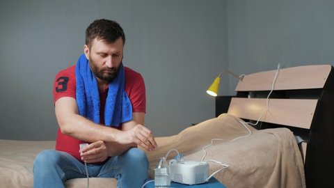 Man screws inhalation mask to nebulizer. Young man sits alone in room and fastens mask to inhaler. Slow motion and general plan