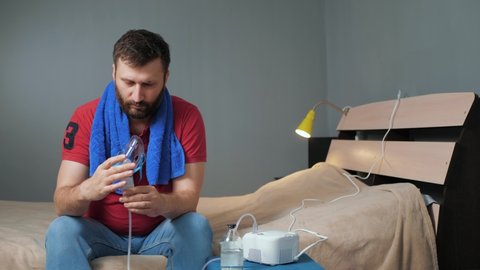 Man puts on mask for inhalation and turns on nebulizer. Young man sits alone in room and puts on mask for inhalation and then presses power button on device. Slow motion and general plan