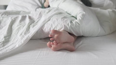 A close-up of the children's feet on the white bed in the morning under the blanket.