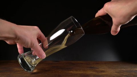 Pour Beer out of a Bottle in a glass on black Background