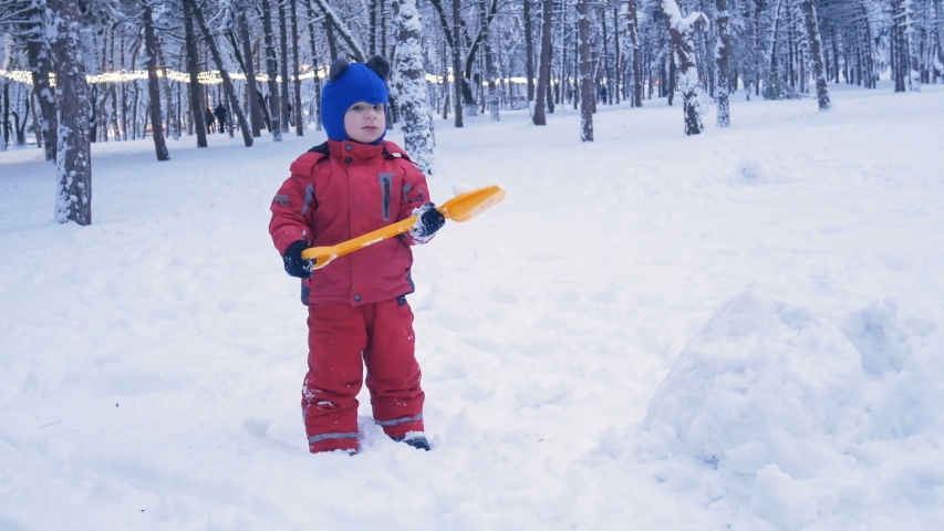 Little boy wearing in red jumpsuit plays with snowballs in snowy winter day, cute happy child  in winter time