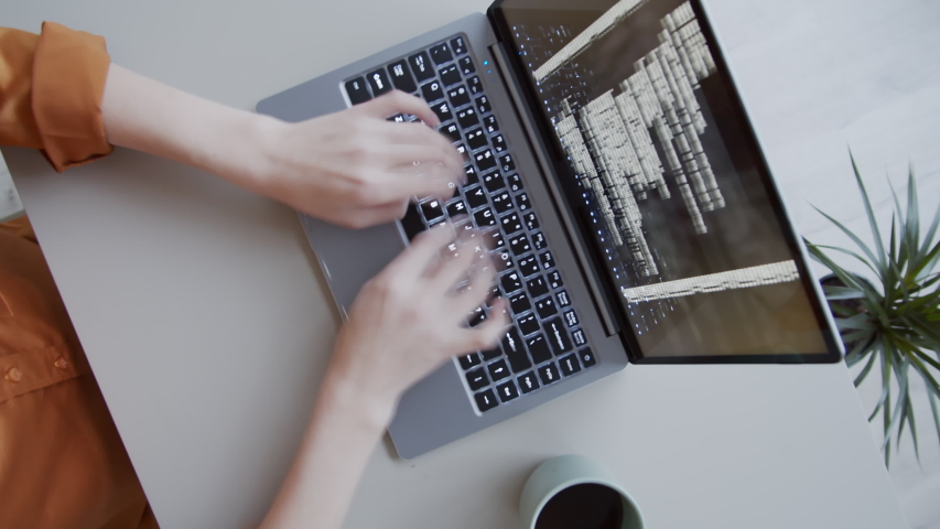 Timelapse top shot of hands of anonymous female programmer sitting and working at desk in office, typing computer code on laptop keyboard, and lines of digital symbols running on screen Royalty-Free Stock Footage #1045020574