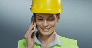 Close up of the young Caucasian beautiful and cheerful woman constructor in the yellow hard helmet talking on the mobile phone and laughing.