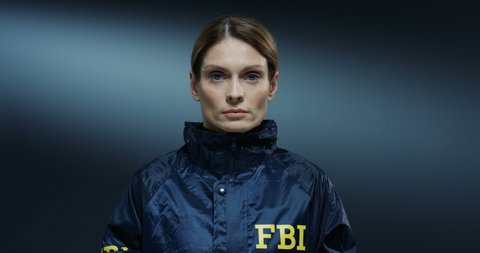 Portrait shot of the beautiful young Caucasian policewoman from FBI looking straight at the camera on the dark backgrond wall.