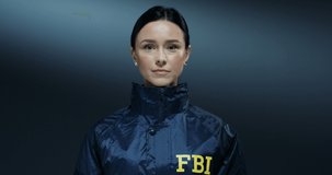 Portrait of the beautiful young Caucasian FBI policewoman in the dark blue uniform looking straight to the camera with serious face. Close up.