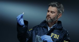 Caucasian man FBI investigator in gloves and uniform putting an evidence and proof of crime - cigarette butts in the plastic bag.