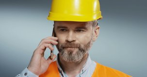 Caucasian grey-haired man constructor in the yellow hard helmet talking on the mobile phone and solving some problems. Close up.