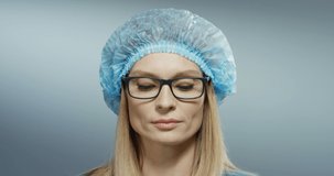 Close up of the young blond good looking woman doctor with serious face in blue hat and glasses looking at the camera. Portrait.