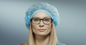 Portrait of the Caucasian beautiful woman physician in glasses, blue hat smiling joyfully to the camera. Close up.