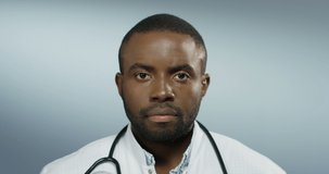Portrait of the young African American good looking man physician looking straight to the camera on the grey wall background. Close up.