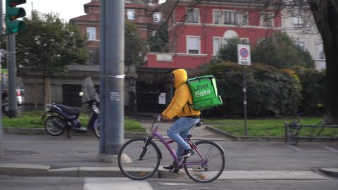 Italy , Milan January 21,2020 - Uber eats delivery food - bike driver going in a street with green bag box  for food , continues during n-cov19 emergency pandemic in Europe and America (USA) and Asia