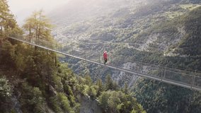 Female hiker with backpack walking on a suspension bridge above a valley in Swiss Alps mountain, scenic landscape for trekking with forest and sun in Switzerland, bisse de Saviese Torrent Neuf, 4k