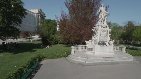 VIENNA AUSTRIA AUGUST 22. 2019 Wolfgang Amadeus Mozart monument, camera is flying around a chestnut tree towards the Mozart memorial in city center of Vienna Austria, people sitting around, no sound