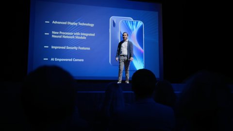 Live Event with Brand New Products Launch: Keynote Speaker Reveals Smartphone Device to the Audience. Movie Theater Screen Shows Mock-up Touch Screen Mobile Phone with High-End Features,  Highlights
