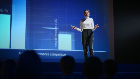 On Stage, Successful Female Speaker Presents Technological Product, Uses Remote Control for Presentation, Showing Infographics, Statistics Animation on Screen. Live Event  Device Release. Slow Motion