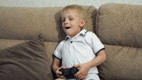 Close-up of a small child five years old playing computer video games at home on the couch. A child with a joystick in his hands enthusiastically plays video games at home. 4K.