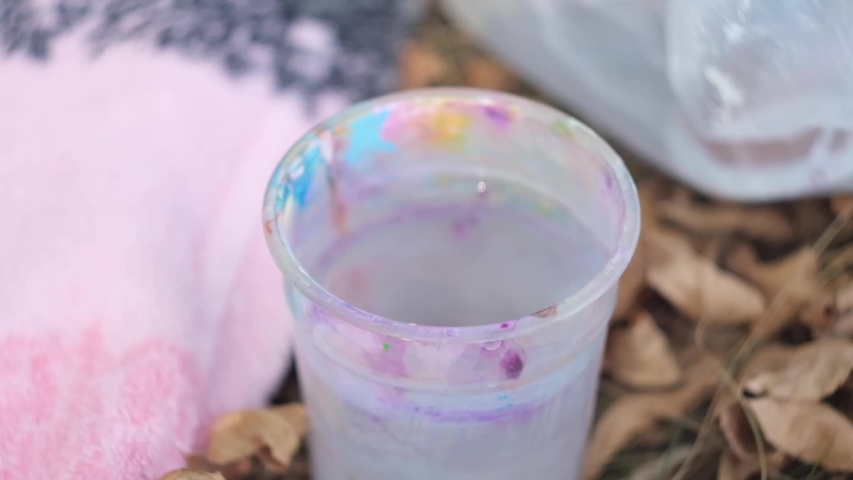 Transparent plastic glass of water mudded by paint brushes