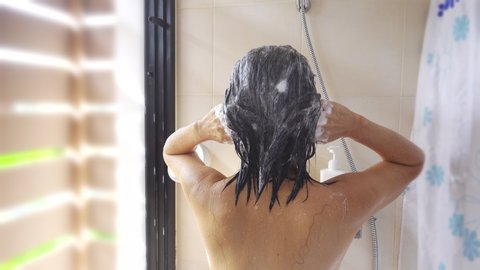 Middle aged asian woman with shorted  black hair takes shower, washing hair in a bath,4K video. 
Mature woman washing her hair with shampoo,upper body rear view. 
Hair massage, beauty and spa concept.