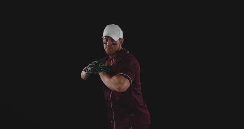 Front view of a Caucasian male baseball pitcher throwing a baseball, slow motion, on black background shot in the studio