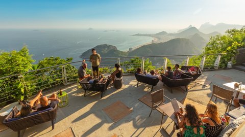 Rio de Janeiro, Brazil - January 18, 2020: Timelapse of crowded rooftop bar restaurant on top of Sugarloaf mountain. View of people drinking. Ocean, Copacabana and Ipanema beach in background.