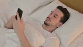 Young Man doing Video Chat on Smartphone in Bed