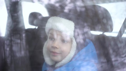 little boy rides in the car in the back seat in winter forest and looks out the window.