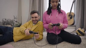 Camera moving up, cute African American girl losing in video game, Caucasian winner smiling and hugging his upset girlfriend. Lifestyle, leisure, gaming.