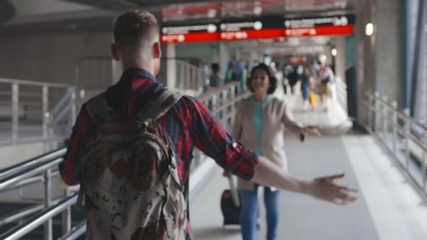 Young hipster man meeting his senior mother in airport walkway. They are greeting each other and hugging. Happy reunion of aged woman and her adult son.